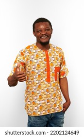 Smiling Black Man With Thumbs Up Hand Gesture In African Bright Clothes Isolated On White Background, Casual African Wear. Nice Bearded Black Guy Portrait With Excited Funny Emotions