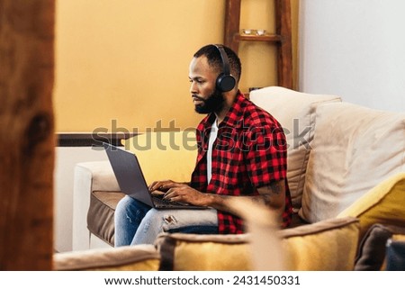 Smiling black man working remotely from home with laptop computer and headphones. Telecommuting and home office concept.