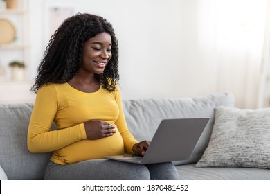 Smiling black pregnant lady using laptop at home, sitting on couch at living room, empty space. Happy african american expecting woman surfing on Internet, reading blog about maternity or shopping - Powered by Shutterstock