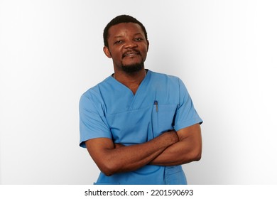 Smiling Black Surgeon Doctor Bearded Man In Blue Coat With Crossed Arms Isolated On White Background. Happy Adult Black African American Practicing Surgeon Portrait, Confident Look