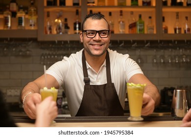 smiling black waiter serves cocktails to customers at the bar, close up - Powered by Shutterstock