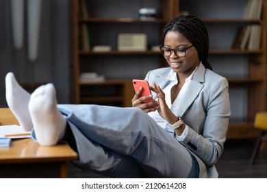 Smiling black woman freelancer using phone at workplace, relaxed african female employee with smartphone procrastinating at work, scrolling through social media during working hours, selective focus