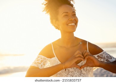 Smiling black woman making heart shape with hands while relaxing on beach in the early morning. Happy african american woman making heart gesture on the beach at sunset. Young beautiful woman at sea. - Shutterstock ID 2151833737