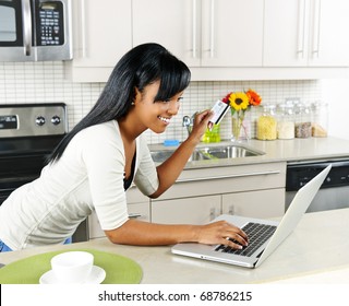 Smiling Black Woman Online Shopping Using Computer And Credit Card In Kitchen