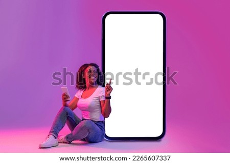 Smiling Black Woman With Smartphone In Hand Sitting In Neon Light And Pointing At Huge Blank Telephone Screen, Happy African Female Recommending New Mobile Application, Creative Collage, Mockup