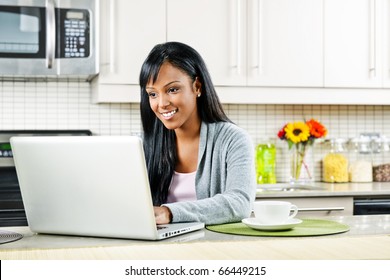 Smiling Black Woman Using Computer In Modern Kitchen Interior