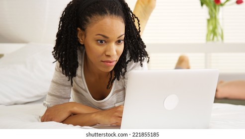 Smiling black woman using laptop on bed - Shutterstock ID 221855185