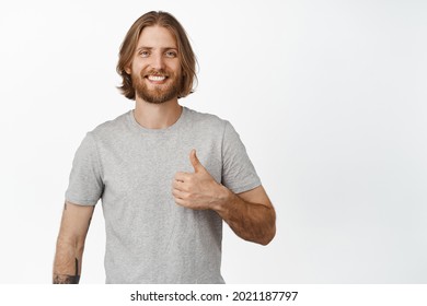Smiling blond man showing thumb up, approve and nod, like something good, excellent choice, praise, making compliment, standing over white background - Shutterstock ID 2021187797