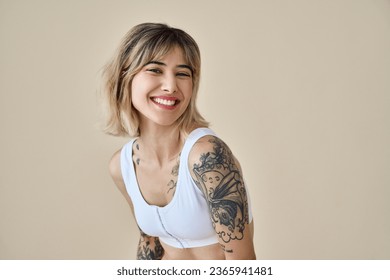 Smiling blond pretty happy girl beauty female generation z tattooed model with short blonde hair beautiful face healthy skin looking at camera laughing isolated at beige background. Aesthetic portrait