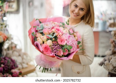smiling blond woman holds great bouquet of pink chrysanthemum hydrangea and roses wrapped in paper. Floral shop concept. Handsome fresh bouquet.