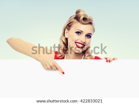 smiling blond woman in pin-up style dress, showing blank signboard with copyspace. Caucasian blond model posing in retro fashion and vintage concept studio shoot.