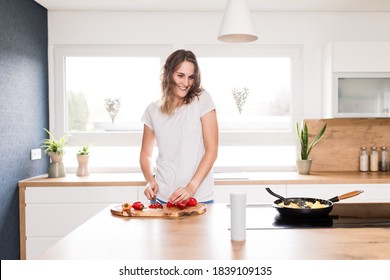 Smiling Blond Woman Talking To Voice Assistant While Cutting Pepper On Kitchen Island At Home