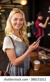 Lächeln Sie blonde Kaffee trinken und verwenden Sie Smartphone in der Cafeteria