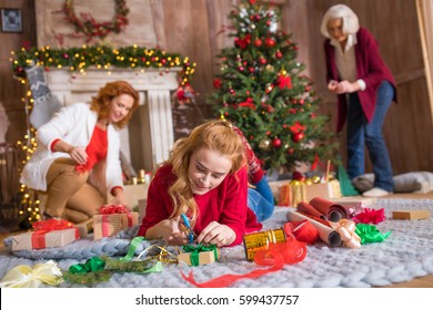 Smiling Blonde Girl Lying On Carpet And Wrapping Gift Box