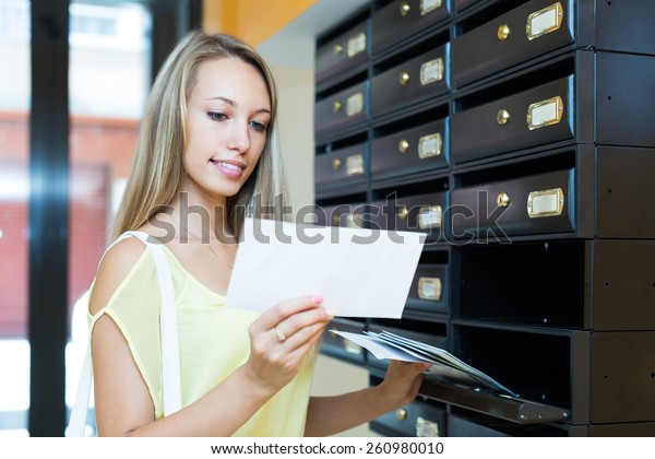 Smiling\
blonde girl taking junk mail out the posting\
box
