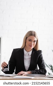 Smiling Blonde Notary Holding Stamper And Looking At Camera While Working In Office