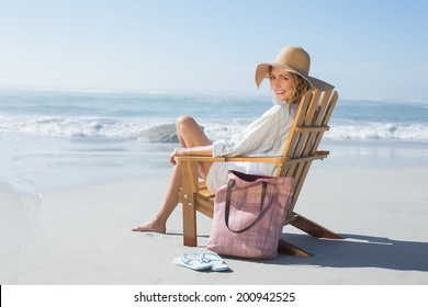 Smiling blonde sitting on wooden deck chair by the sea on a sunny day - Powered by Shutterstock