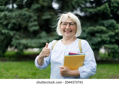 Smiling Blonde Teacher Woman Lady 40s 50s Years Old Wearing Eyeglasses Standing Hold Notepads Showing Thumbs Up Looking Camera Outdoors