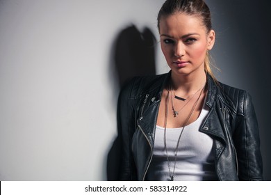 Smiling Blonde Woman In Leather Jacket Standing Near Grey Wall In Studio