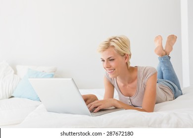 Smiling blonde woman using laptop at home in bedroom. Working from home in quarantine lockdown. Social distancing Self Isolation - Powered by Shutterstock