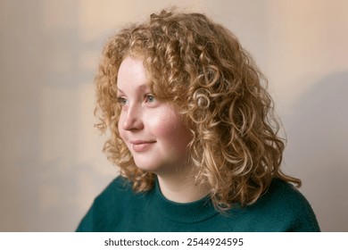 Smiling blonde young woman. Dreamy girl with curly voluminous red hair. Portrait in studio. Natural light filtering in through a window. Pastel background. - Powered by Shutterstock