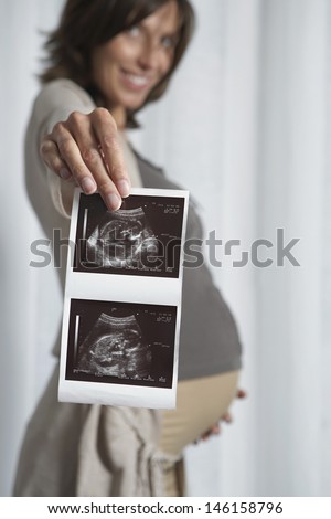 Smiling blurred pregnant woman holding out ultrasound scan photo of baby