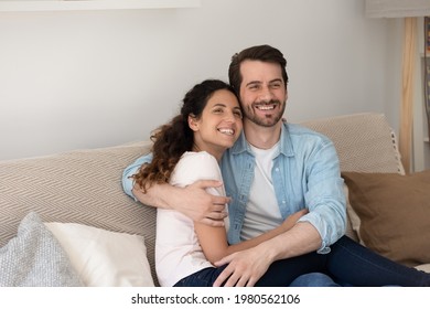 Smiling Bonding Young Family Couple Relaxing On Comfortable Couch, Watching Smart Television Programs, Enjoying Stress Free Leisure Weekend Time Together In Living Room, Entertainment Activity Concept