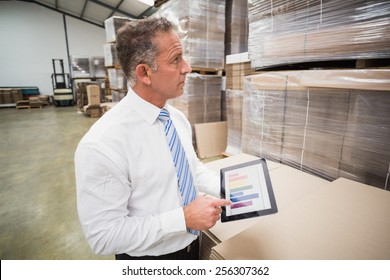 Smiling boss using tablet pc in a large warehouse