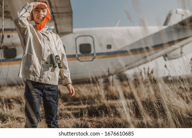 Smiling boy in aviator hat posing near airplane outdoors stock photo
