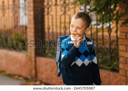 Smiling boy with backpack eats sandwich outdoors before school, morning routine, healthy snack, back to school season