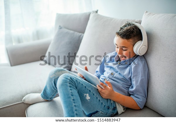 Smiling boy\
in big white headphones watching videos on tablet computer. Little\
boy in headphones is using a digital tablet and smiling.\
Concentrated kid playing with digital\
tablet