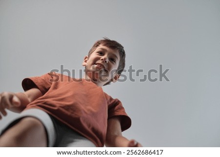 A smiling boy is captured from a low angle, creating a playful and engaging perspective. The image highlights joy, energy, and the curiosity of childhood.