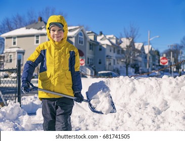 Smiling Boy Is Carrying Snow On A Shovel. Child Cleans The Yard After A Snowfall. Kid Shoveling Snow