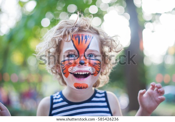 smiling boy with curly hair and face art painting like\
tiger, little boy making face painting, halloween party, child with\
funny face painting, little cute boy with faceart on birthday party\
close up