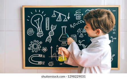 Smiling boy dressed as chemist with flask pointing at a blackboard with drawings