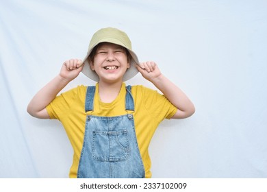 smiling boy dressed in a denim jumpsuit with a yellow shirt, ready to explore the world with his fashionable hat on, his crooked teeth adding charm to his joyful expression