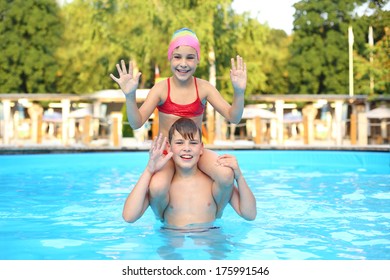 Smiling Boy And Girl Playing In The Outdoor Swimming Pool And Waving Their Hands