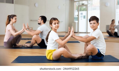 Smiling boy and girl siblings practicing yoga in pair with their parents on mats at gym - Powered by Shutterstock