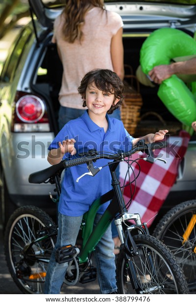 Smiling boy with his\
bike in front of a car