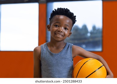 Smiling boy holding basketball in school gym, ready for sports activity. childhood, athletics, enthusiasm, teamwork, fitness, energy - Powered by Shutterstock