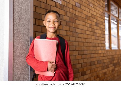 Smiling boy holding folder and wearing backpack in school hallway. education, student, childhood, studying, learning - Powered by Shutterstock