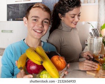 Smiling Boy Holding Fruit Bowl In His Hand While His Mother Cutting Oranges And Making Him A Fresh Orange Juice