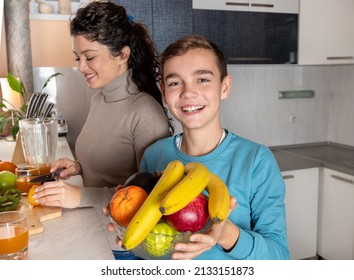 Smiling Boy Holding Fruit Bowl In His Hand While His Mother Cutting Oranges And Making Him A Fresh Orange Juice