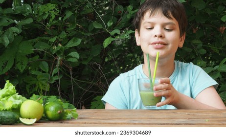 smiling boy holding glass cup a bottle of healthy detox green smoothie spinach, kiwi, apple, lettuce, lime. Happy child drinks a green vitamin juice green foliage, in the garden, in the yard, outdoor. - Powered by Shutterstock