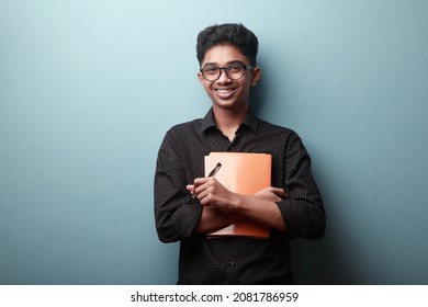 Smiling boy of Indian ethnicity holding note books in his hands