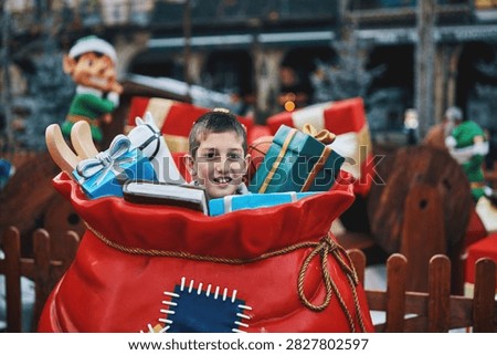 Smiling boy inside Santa sack surrounded by Christmas gifts