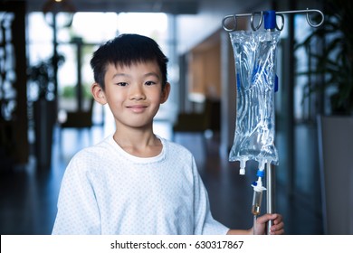 Smiling boy patient holding intravenous iv drip stand in corridor at hospital - Powered by Shutterstock