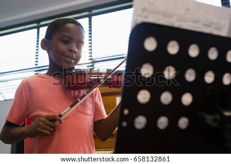 Smiling boy playing violin while standing in classroom at school