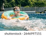 Smiling boy in pool float with blue goggles enjoying fun summer day in backyard swimming pool