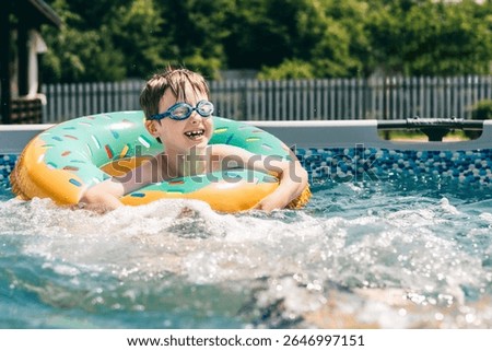 Smiling boy in pool float with blue goggles enjoying fun summer day in backyard swimming pool